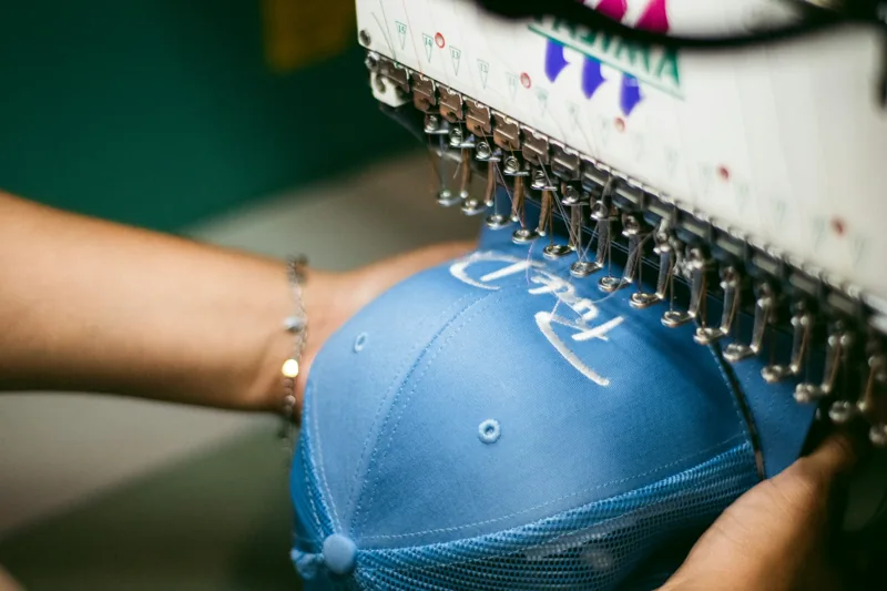 An embroidery machine stitching a custom design onto a cap